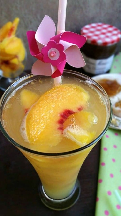 Glass of Pineapple Peach Mimosa with a pink straw and garnished with peaches. 