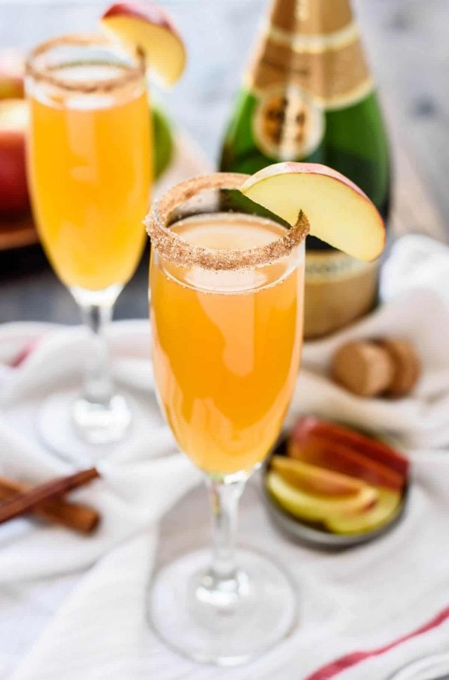 Two Apple Cider Mimosas rimmed with cinnamon and garnished with sliced apples. 