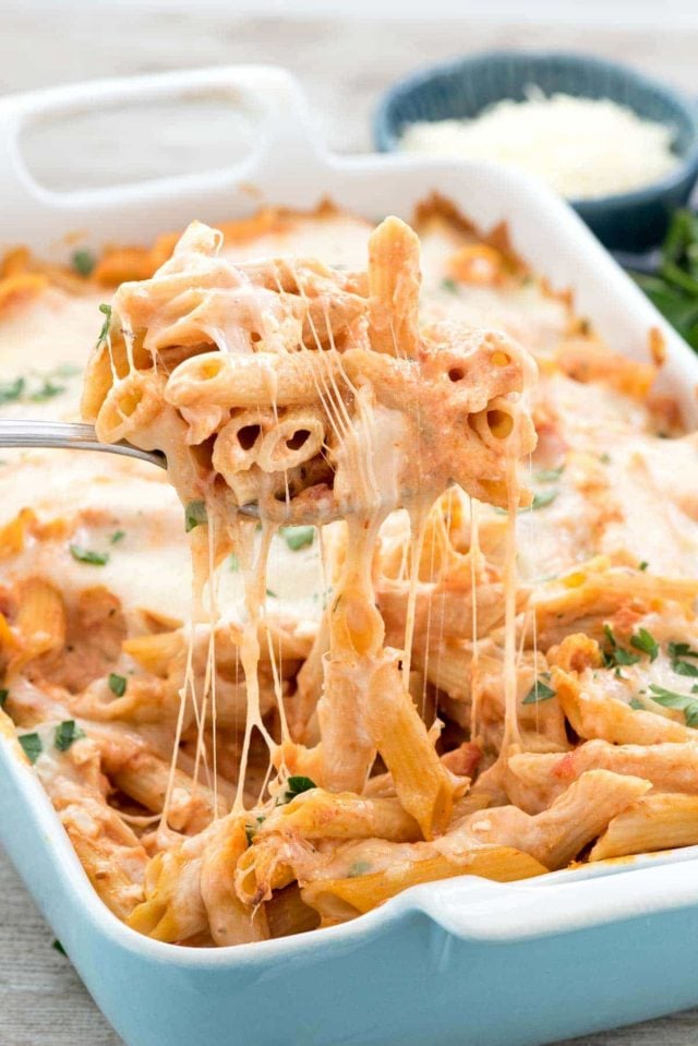 Scooping out Baked Penne out of blue casserole dish.