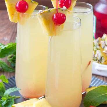 Three Hawaiian Mimosas garnished with cherries and sliced pineapple on a plate.