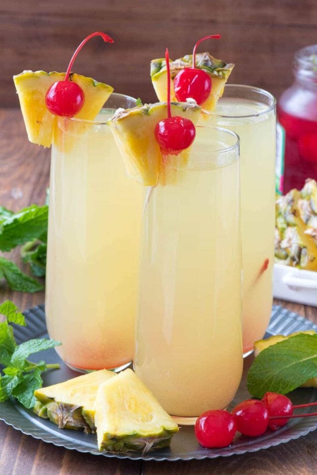 Three champagne glasses of Hawaiian Mimosas garnished with cherries and slice pineapples.