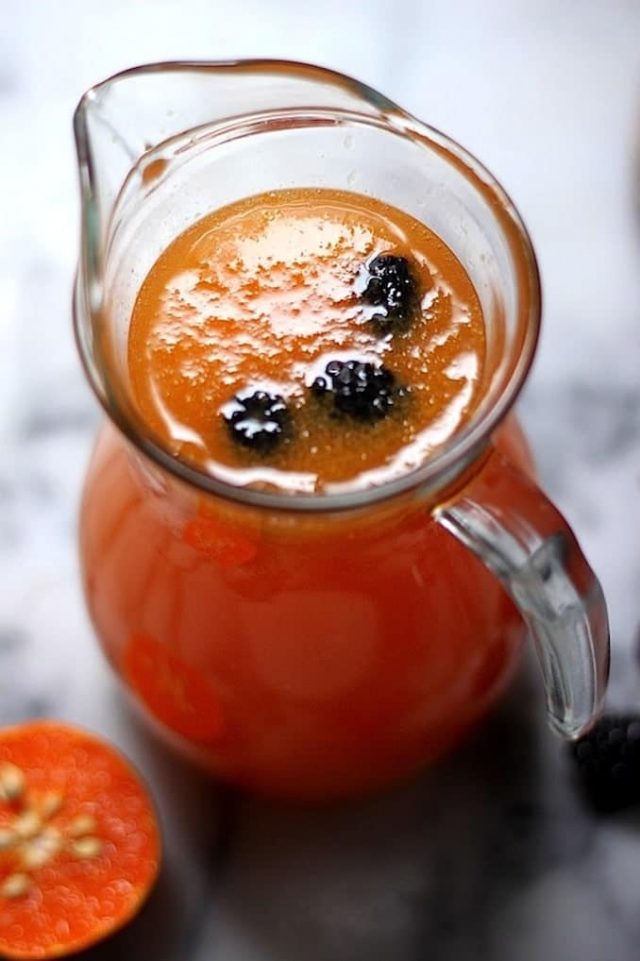 Glass pitcher of Tangerine Mimosas garnished with blackberries.