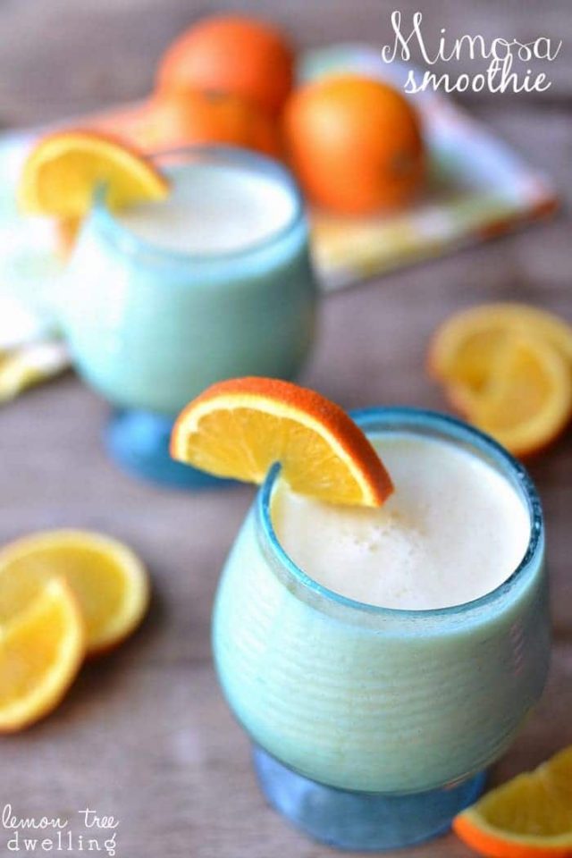 Two Mimosa Smoothies in blue glasses garnished with sliced oranges. 