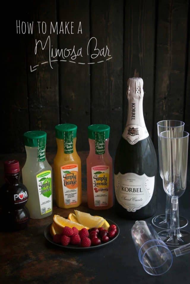 A Mimosa Bar with champagne, simply lemonade, champagne glasses and a plate of cherries, raspberries and sliced oranges. 