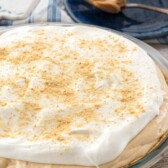 No Bake Peanut Butter Pie in a pie dish with a small dark plate behind with a spoon of Peanut butter