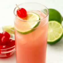 Seabreeze Cocktail Punch in a glass with limes and cherries behind