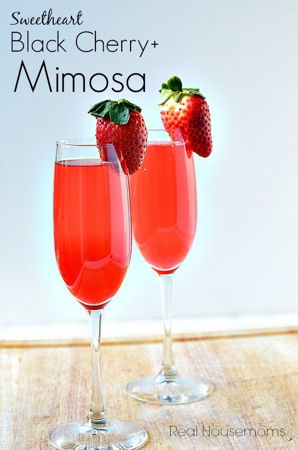 Two champagne glasses of Sweetheart Black Cherry Mimosas garnished with fresh strawberries. 