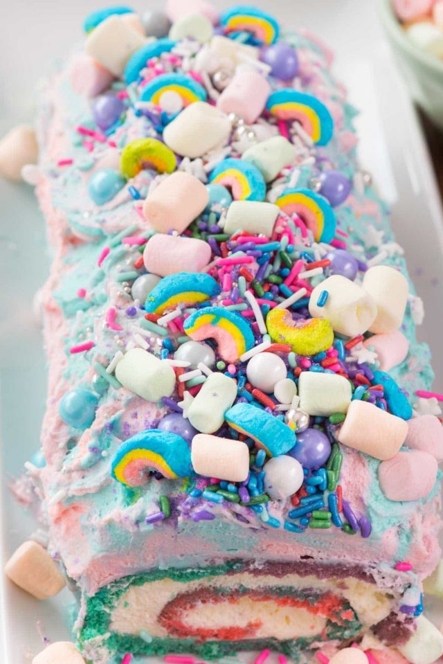 Unicorn Cake Roll with sprinkles and marshmallows on a white serving platter. 