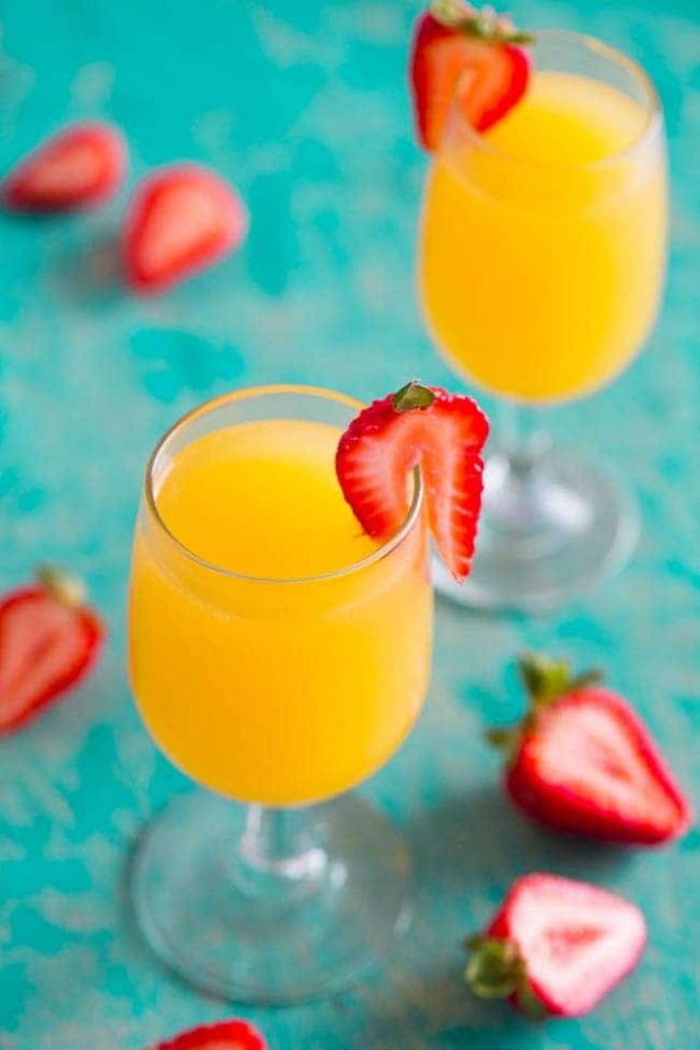 Two drinking glasses of Tropical Mango Mimosas with sliced strawberries. 