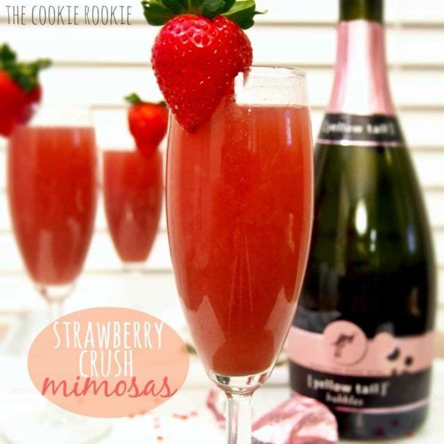 Three champagne glasses of Strawberry Mimosas garnished with fresh strawberries. 