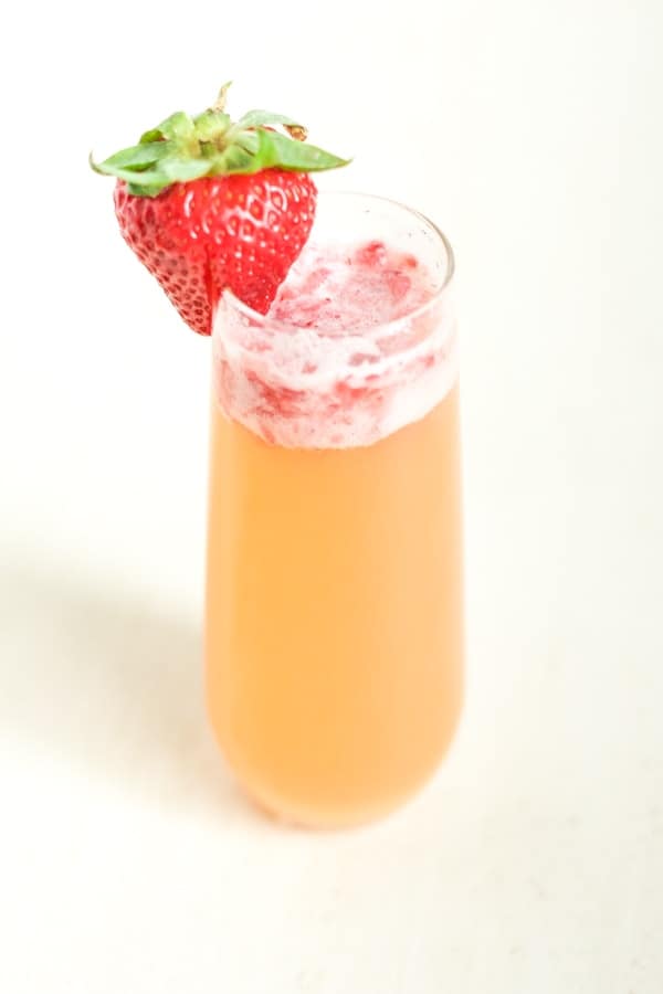 Champagne glass of a Pineapple Strawberry Mimosa garnished with a fresh strawberry. 