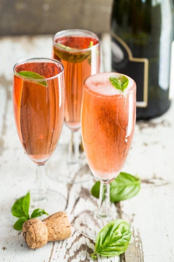 Three champagne glasses of Pomegranate Mimosas with Fresh Basil.