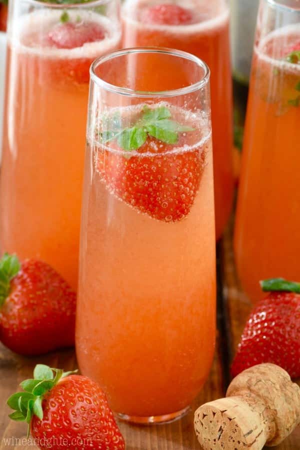 Five champagne glasses of Strawberry Bellini Mimosas garnished with fresh strawberries. 