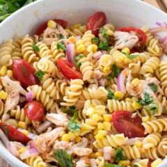 BBQ Chicken Pasta Salad in a white bowl with limes and some cilantro behind it