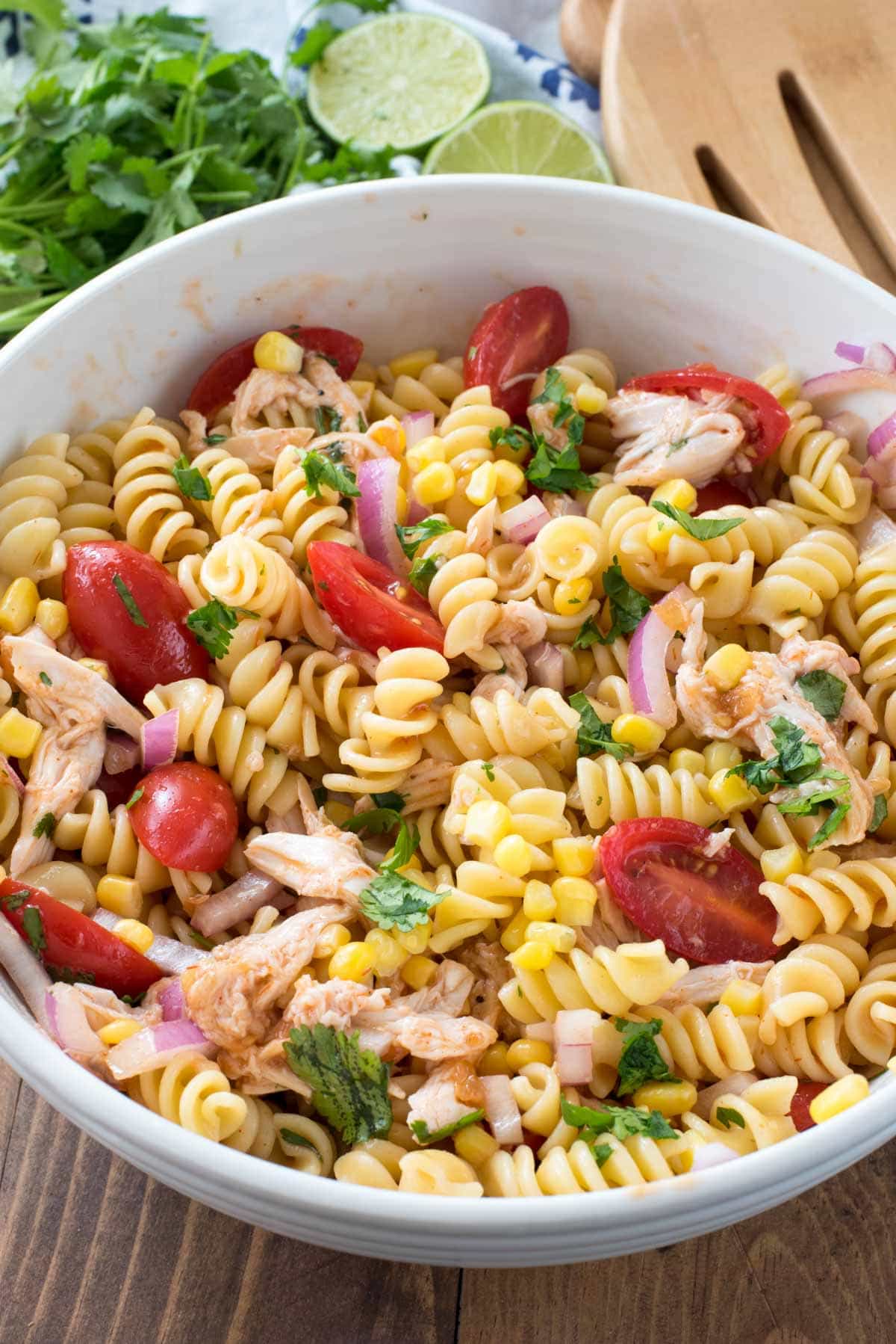 BBQ Chicken Pasta Salad in a white bowl with limes and some cilantro behind it