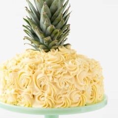 Picture of Pineapple cake with the top of a pineapple on top of the cake A pineapple cake is a frosted 2 layer cake decorated with buttercream icing rosette swirls to make it look like a pineapple! Get the recipe tutorial here!