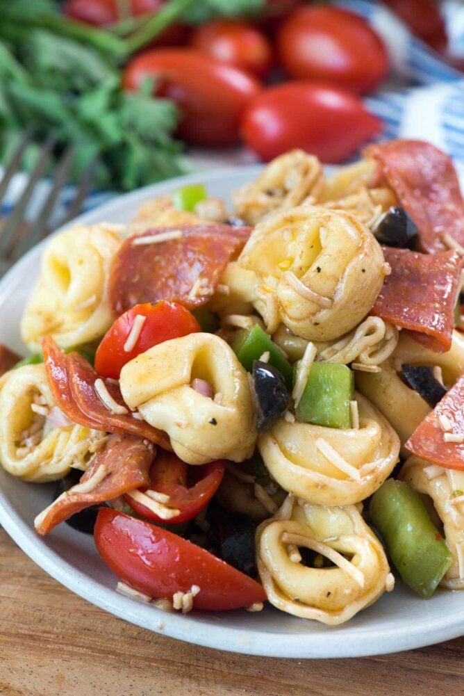 Pizza Tortellini Salad on white plate with vegetables behind