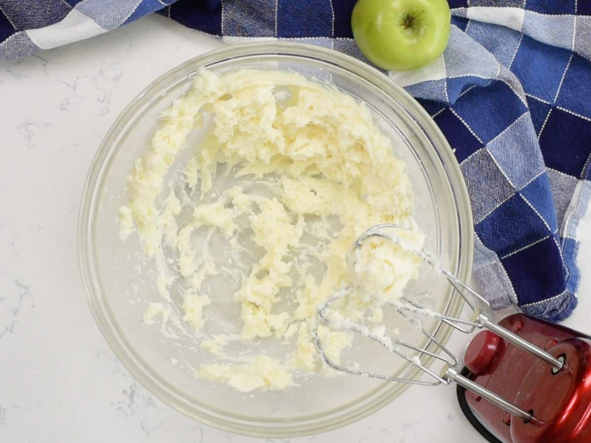 bowl of cheesecake mixture with cream cheese box and apple behind