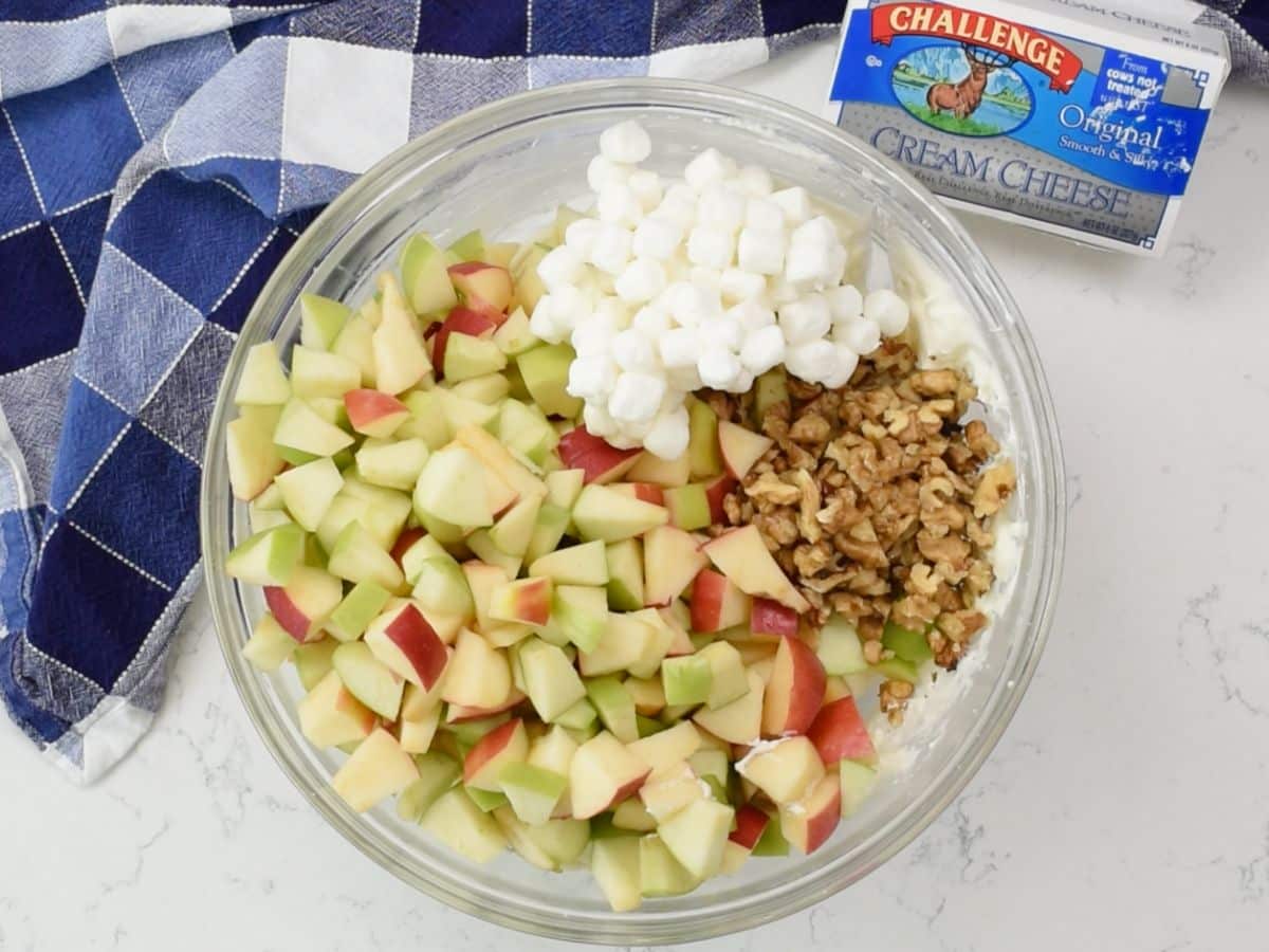 bowl of mixture with apples nuts nad marshmallows with cream cheese box and apple behind