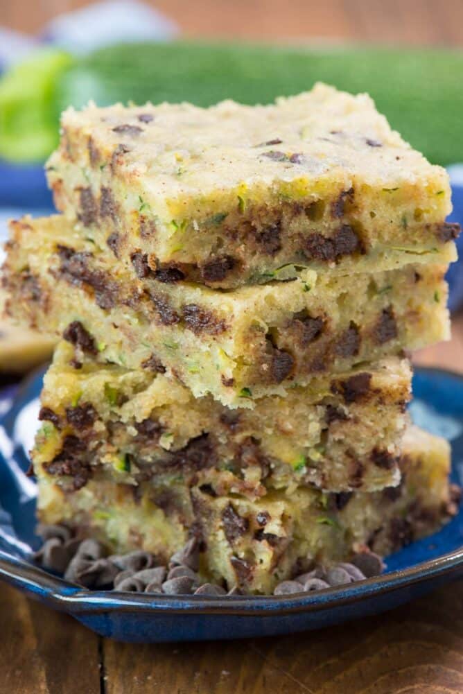 Chocolate Chip Zucchini Bars  in stack on blue plate- this easy one bowl zucchini bar recipe isn't quite a cookie or a cake but it's a delicious soft and sweet dessert full of zucchini and chocolate!