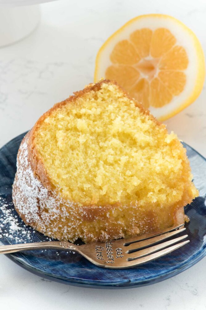 Lemon cake on a blue plate with a fork and a lemon slice