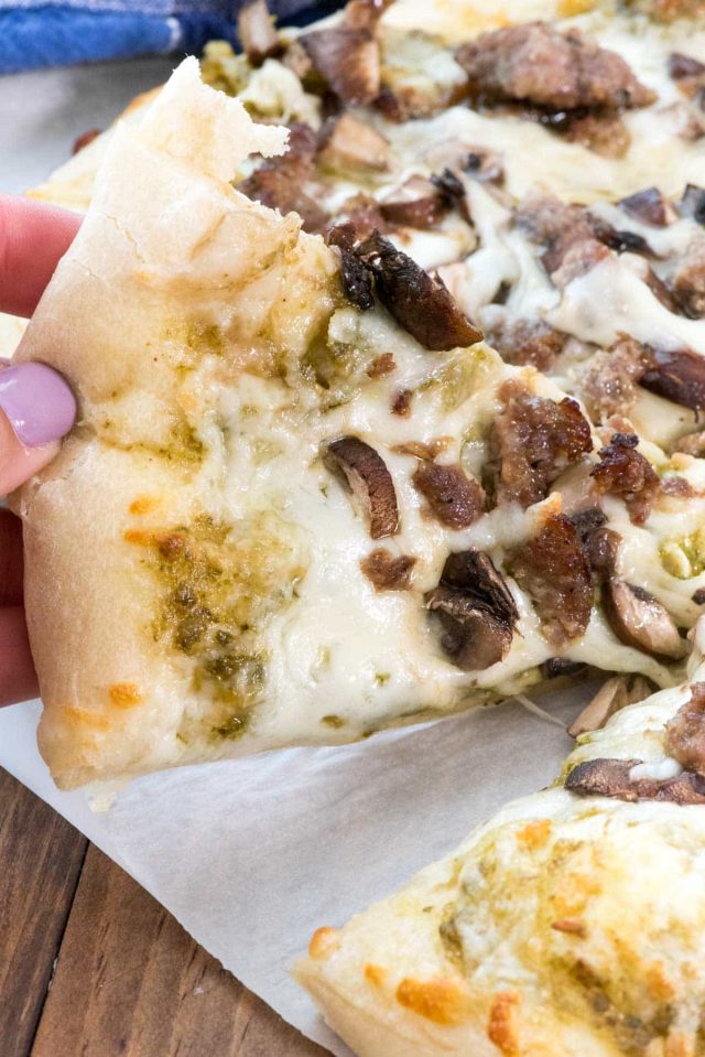 Mushroom Sausage Pesto Pizza with a piece being pulled out by someones hand