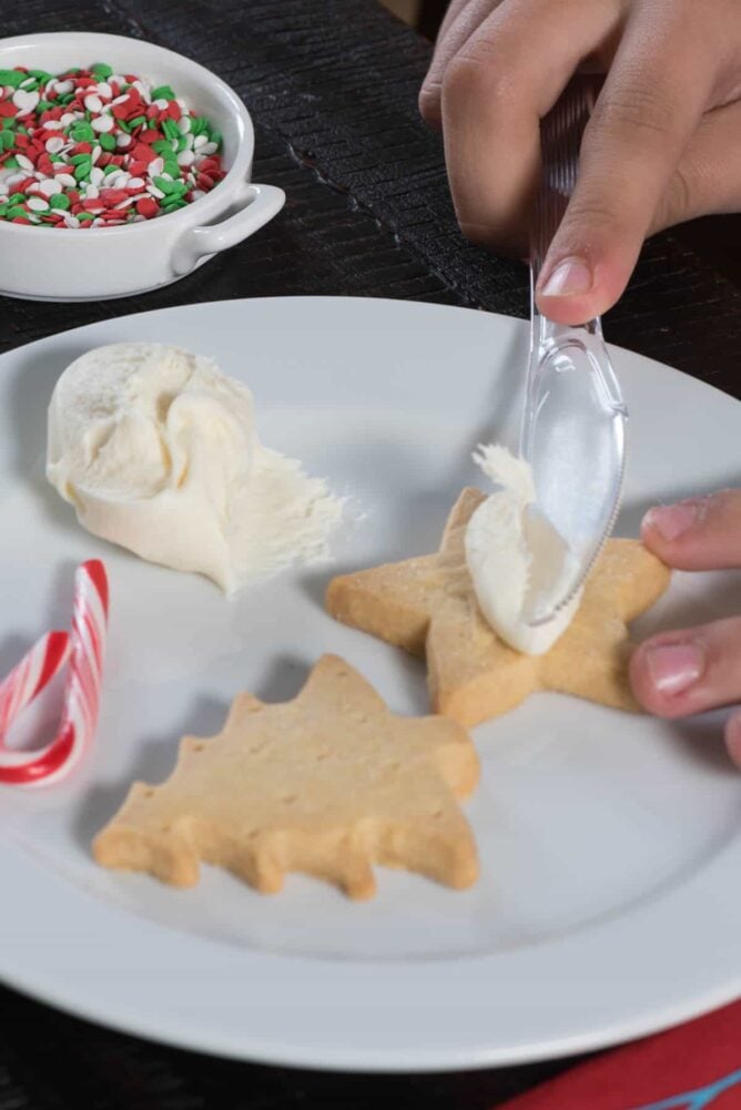 Christmas cookies on a white plate being decorated with frosting