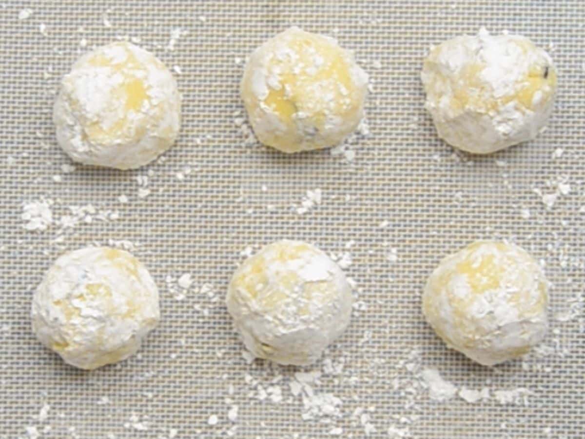 cookie dough balls rolled in powdered sugar on cookie sheet.
