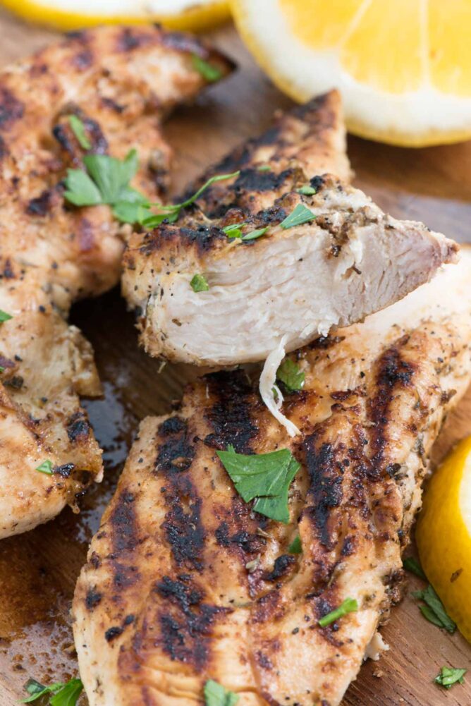 Grilled Lemon Herb Chicken on a cutting board with lemon slices