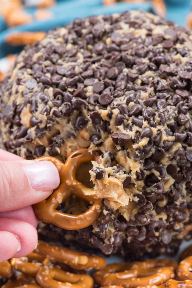 peanut butter cheeseball with finger dipping a pretzel