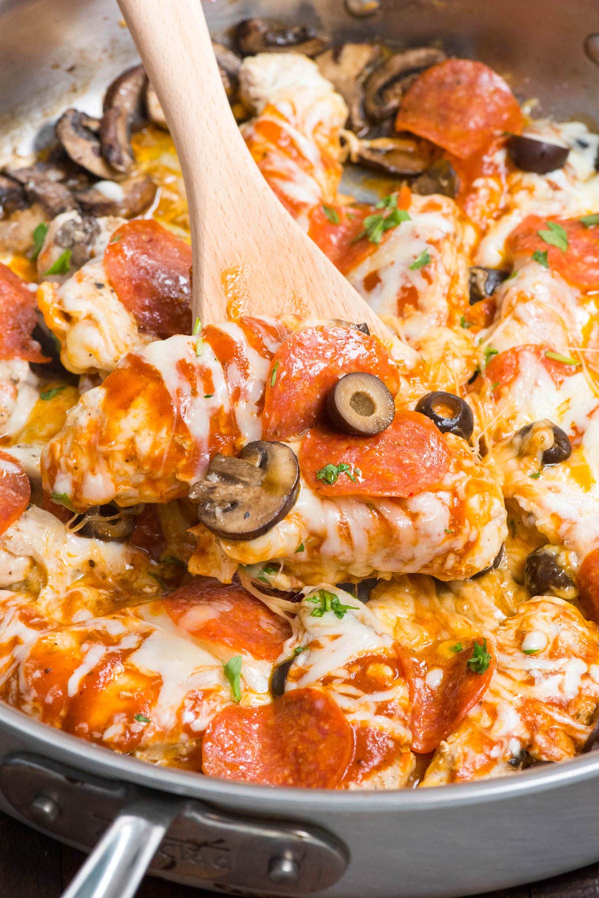 pizza topped chicken in skillet with spoon holding some up