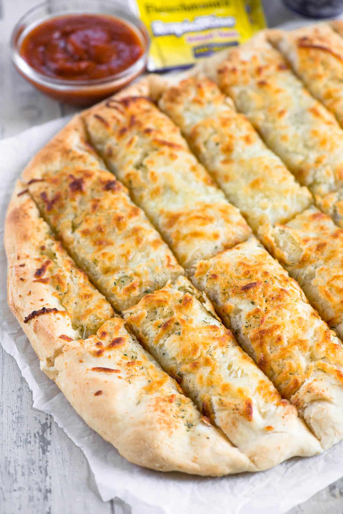 cut breadsticks on parchment with yeast and sauce behind