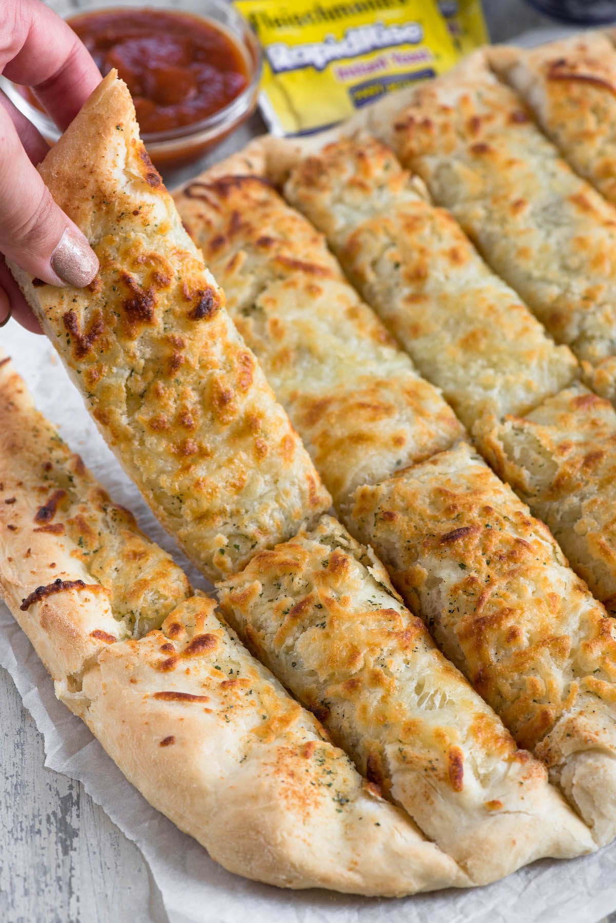 cut breadsticks on parchment with yeast and sauce behind