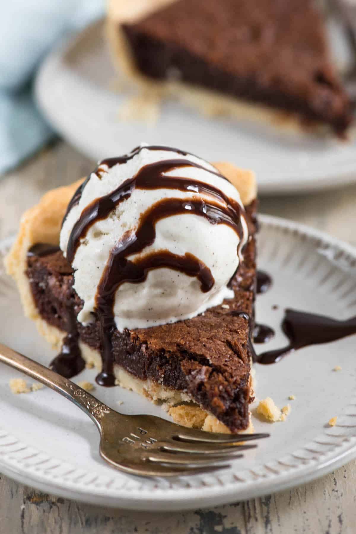 slice of fudge pie with ice cream and chocolate sauce on white plate with fork.