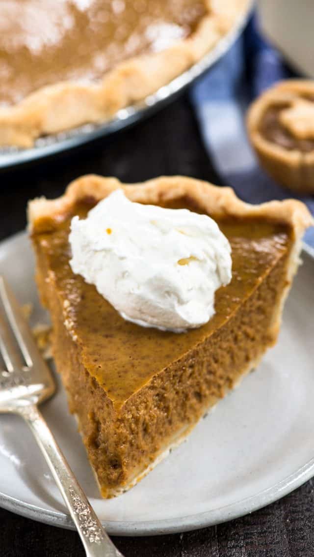 slice of pumpkin pie with whipped cream on a white plate with a fork