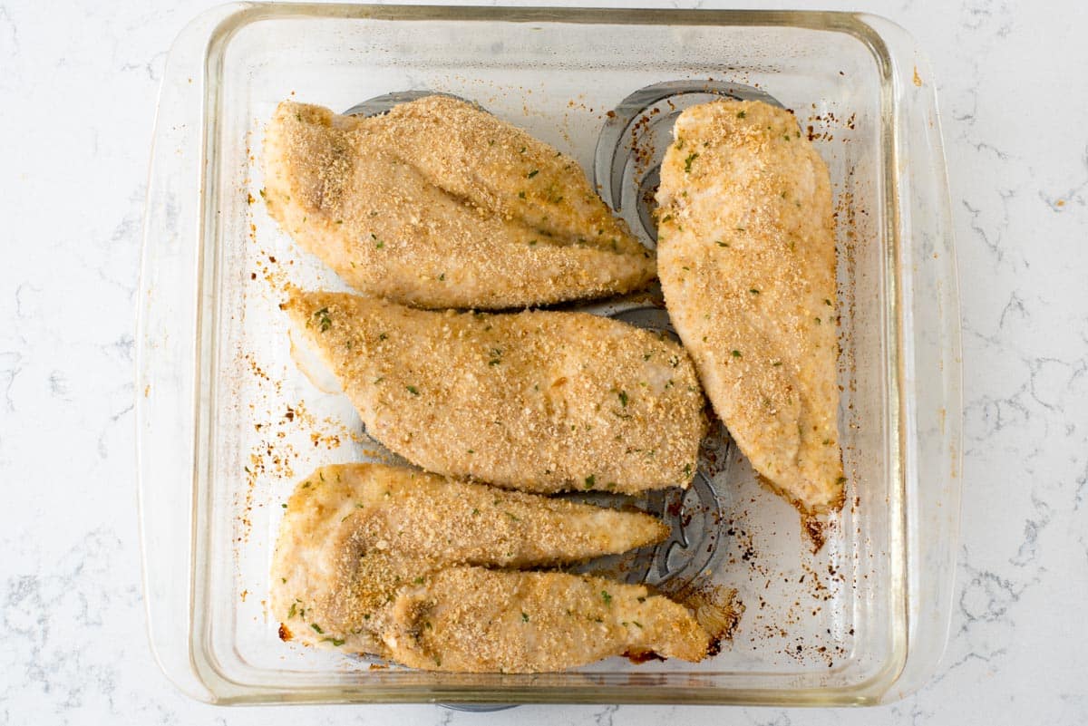 partially baked chicken breasts with breading in pan.