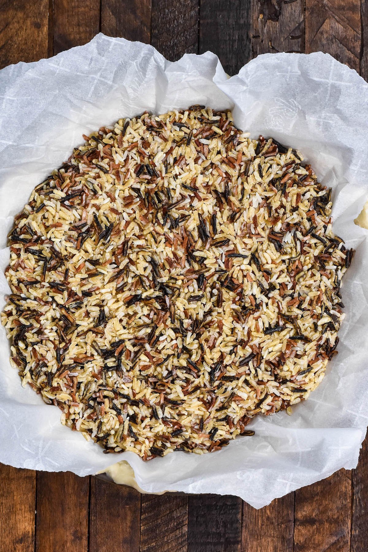 pie crust filled with parchment paper and wild rice on brown background