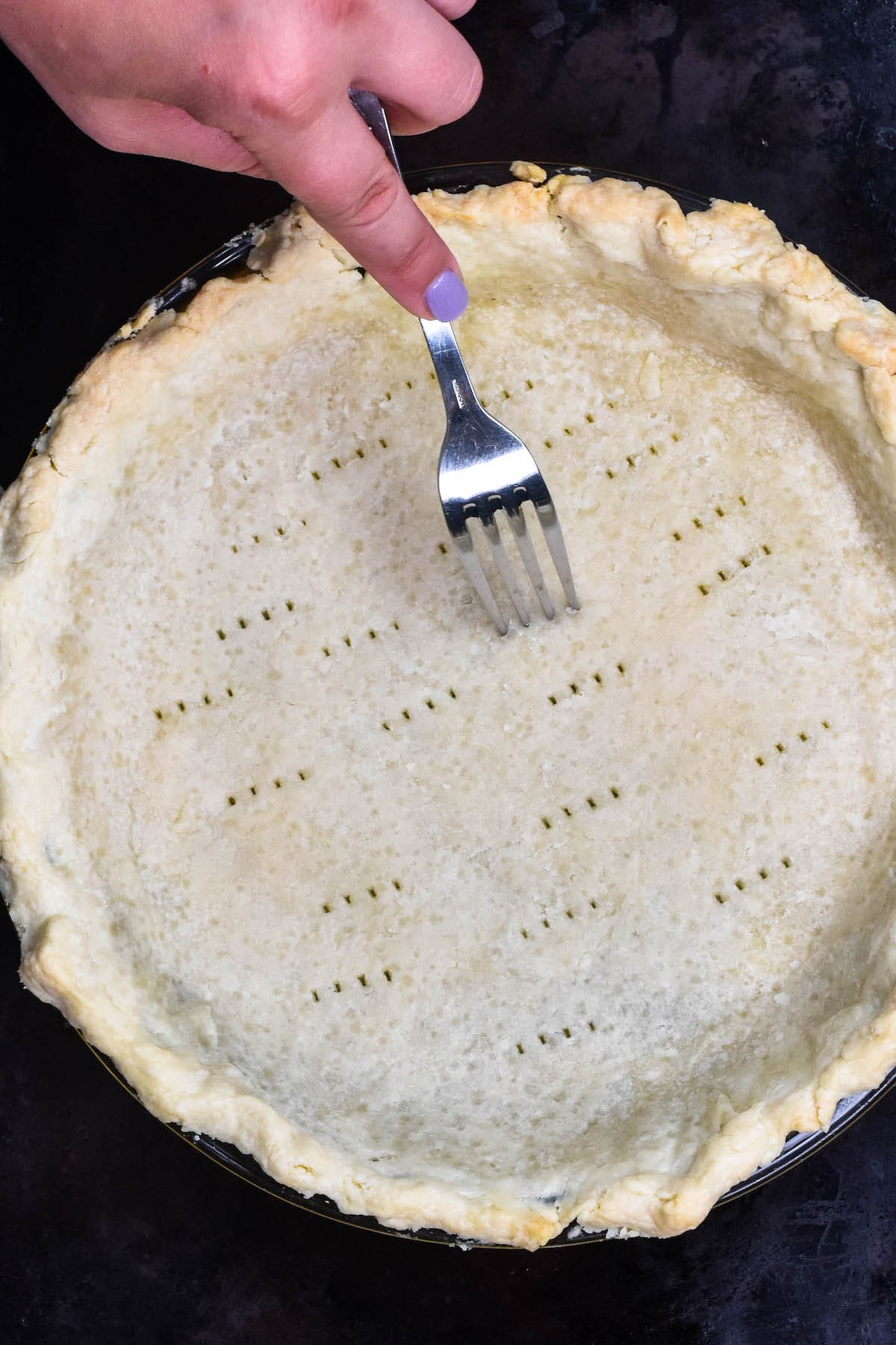 pie crust in pie plate partially baked with hand pressing fork into bottom