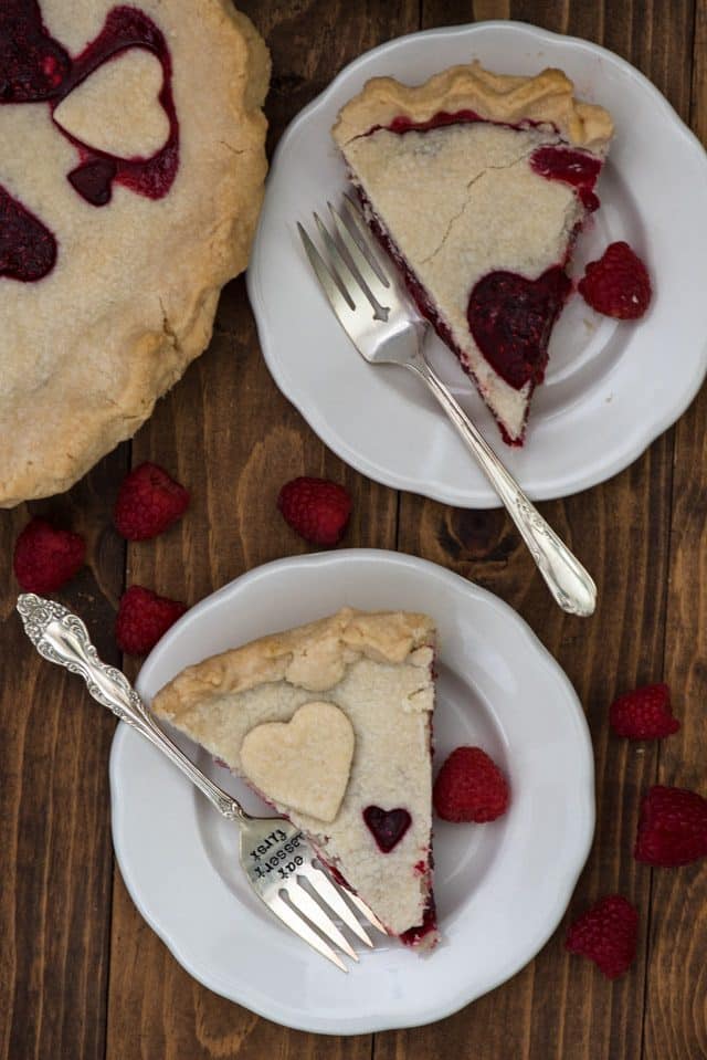 overhead shot of two slices of raspberry pie on white plates with a fork