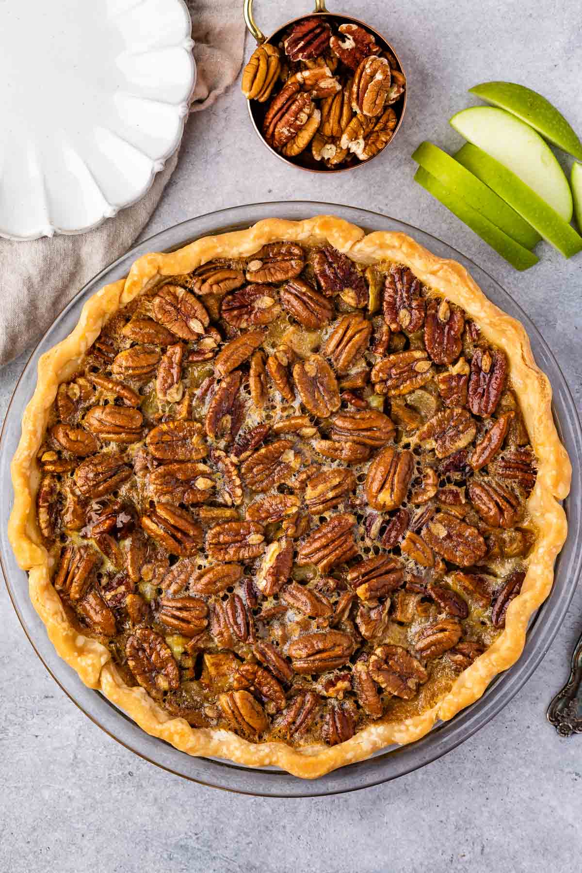 overhead shot of pecan pie with apple slices and cup pecans above