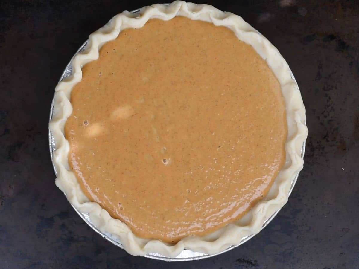 pumpkin pie mixture in unbaked pie shell on cookie sheet.