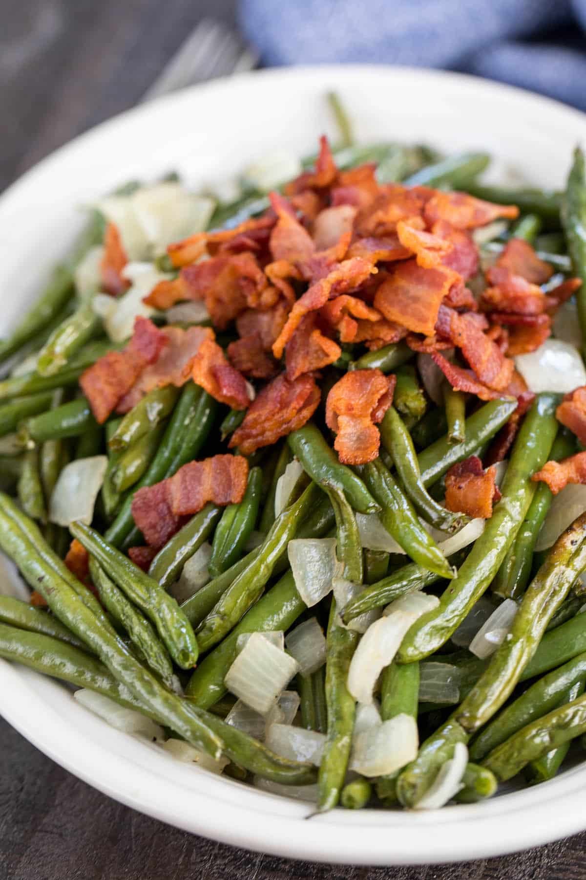 white platter with roasted green beans, onions and bacon.