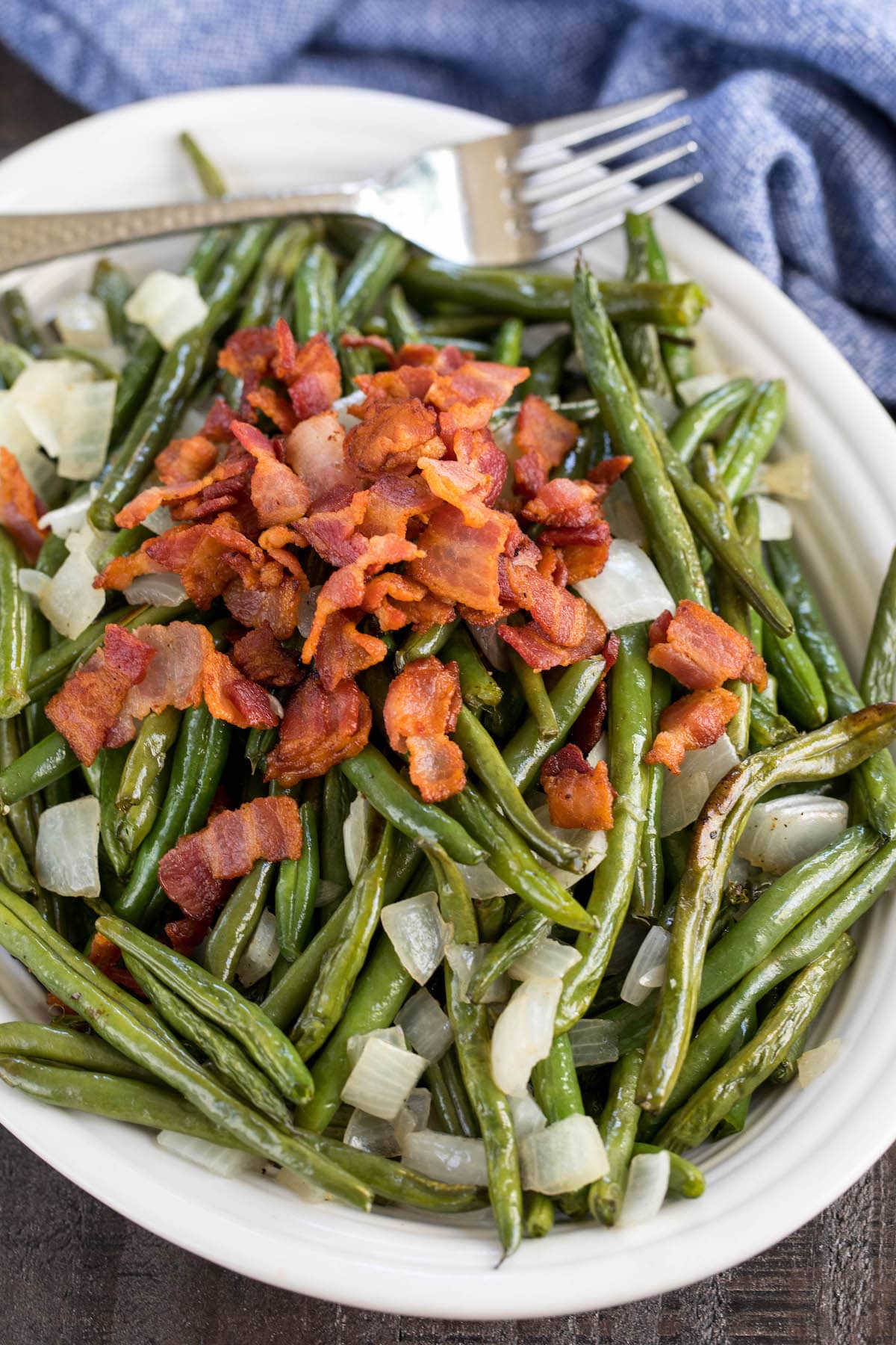 white platter with roasted green beans, onions and bacon.