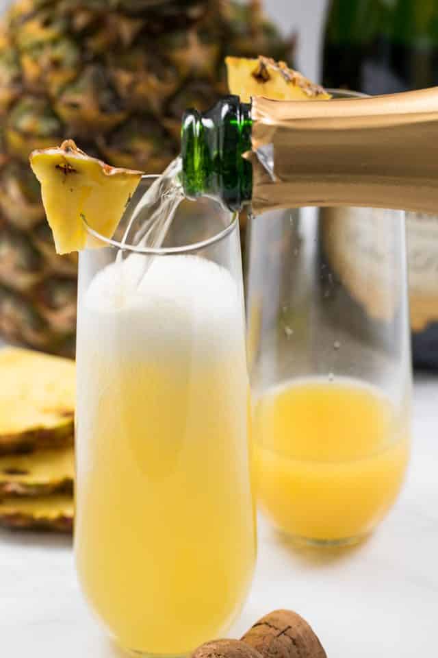 pouring champagne into pineapple mimosa