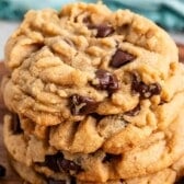 A close-up of a stack of soft, golden-brown peanut butter chocolate chip cookies with fork marks and a chunky texture on a wooden surface.