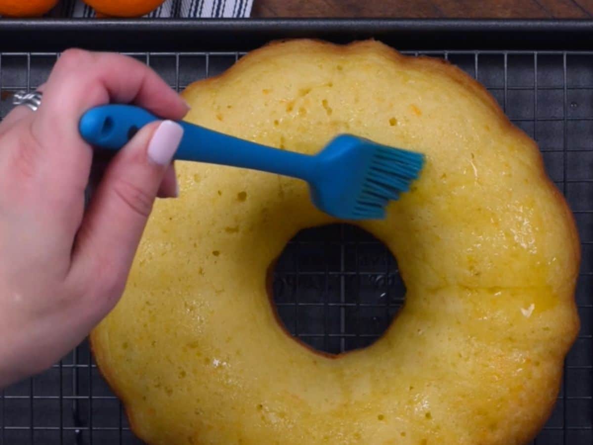 baked cake on rack with hand holding pastry brush.