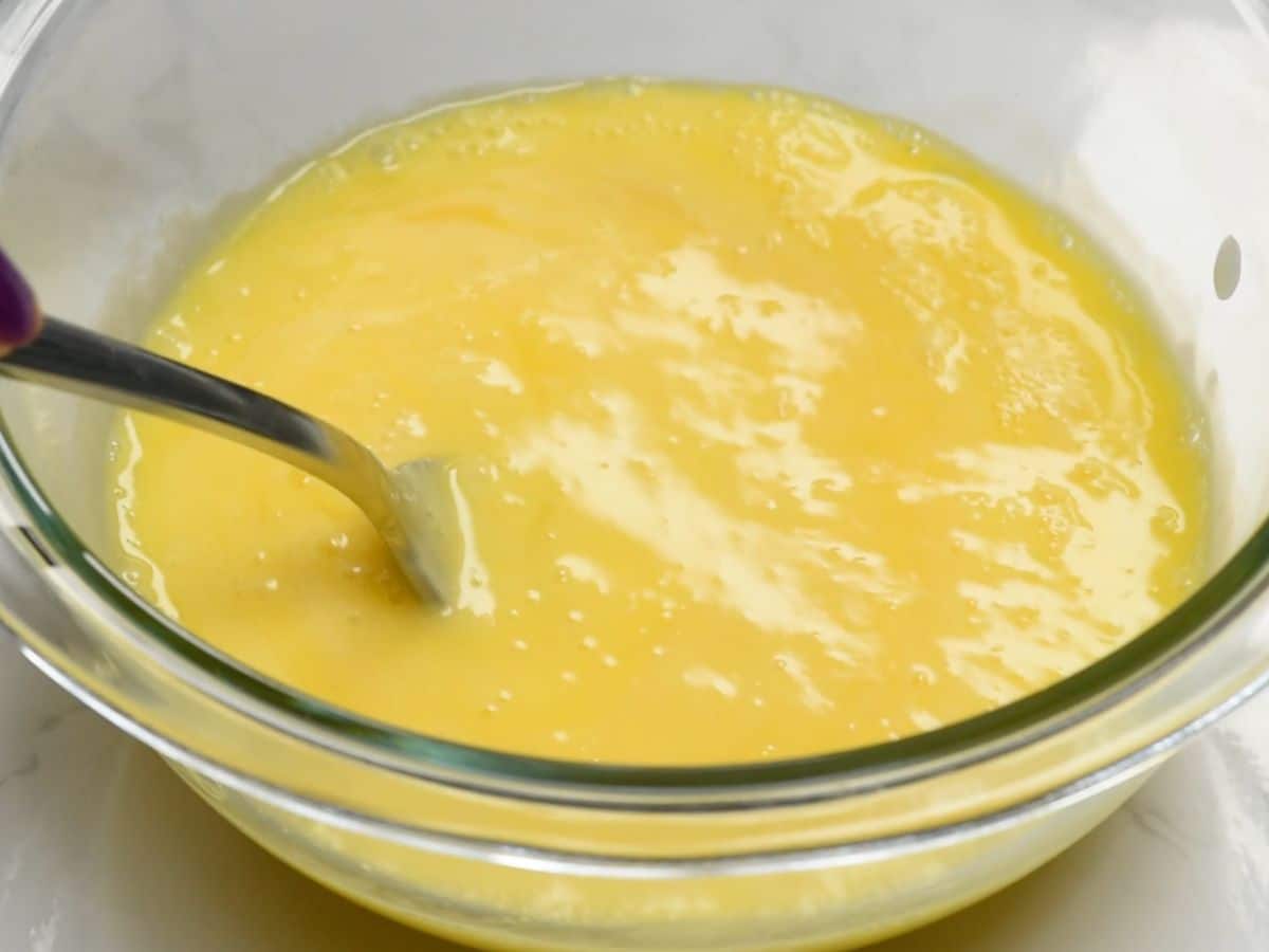 beaten eggs and a bit of milk mixture in glass bowl with fork.