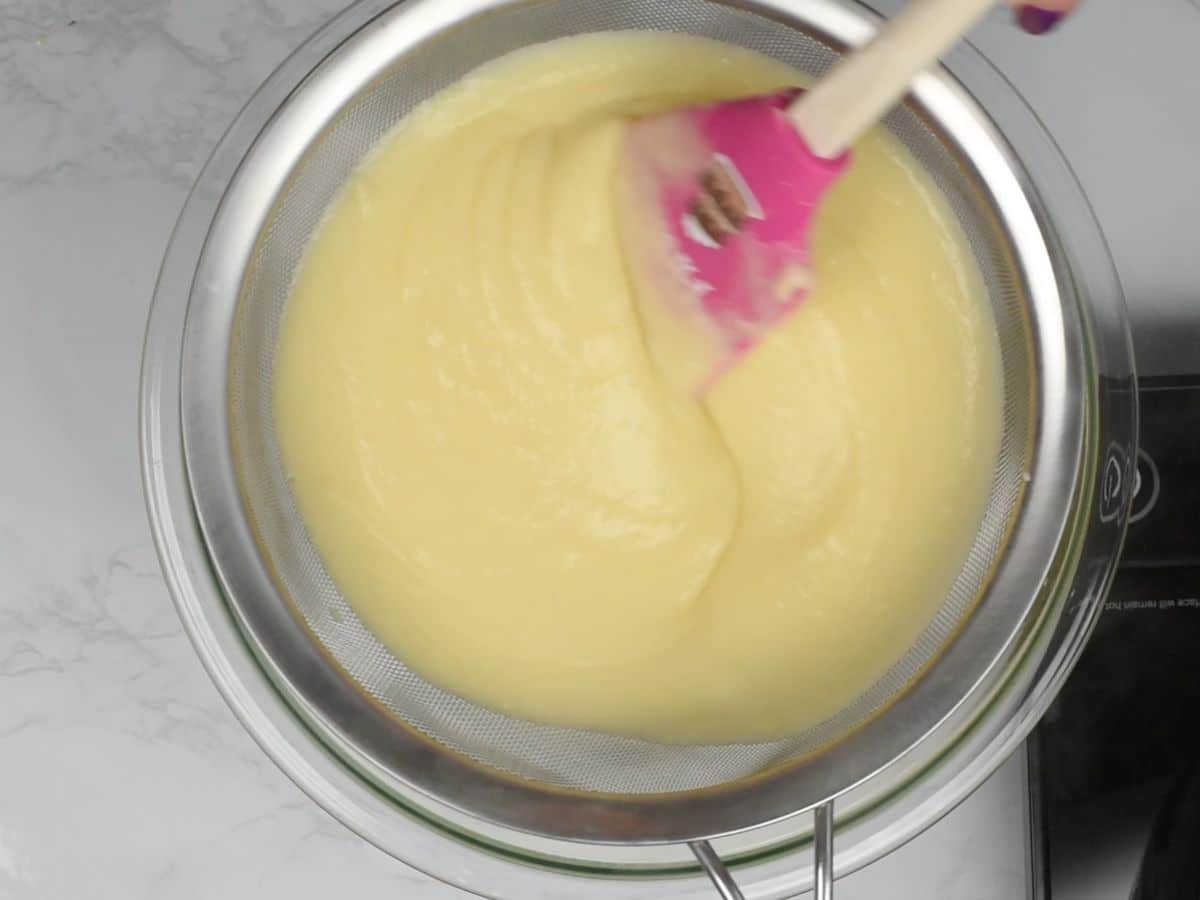 pudding being strained into a bowl with a spatula.