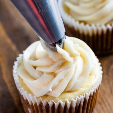 cupcake being frosted with cream cheese frosting