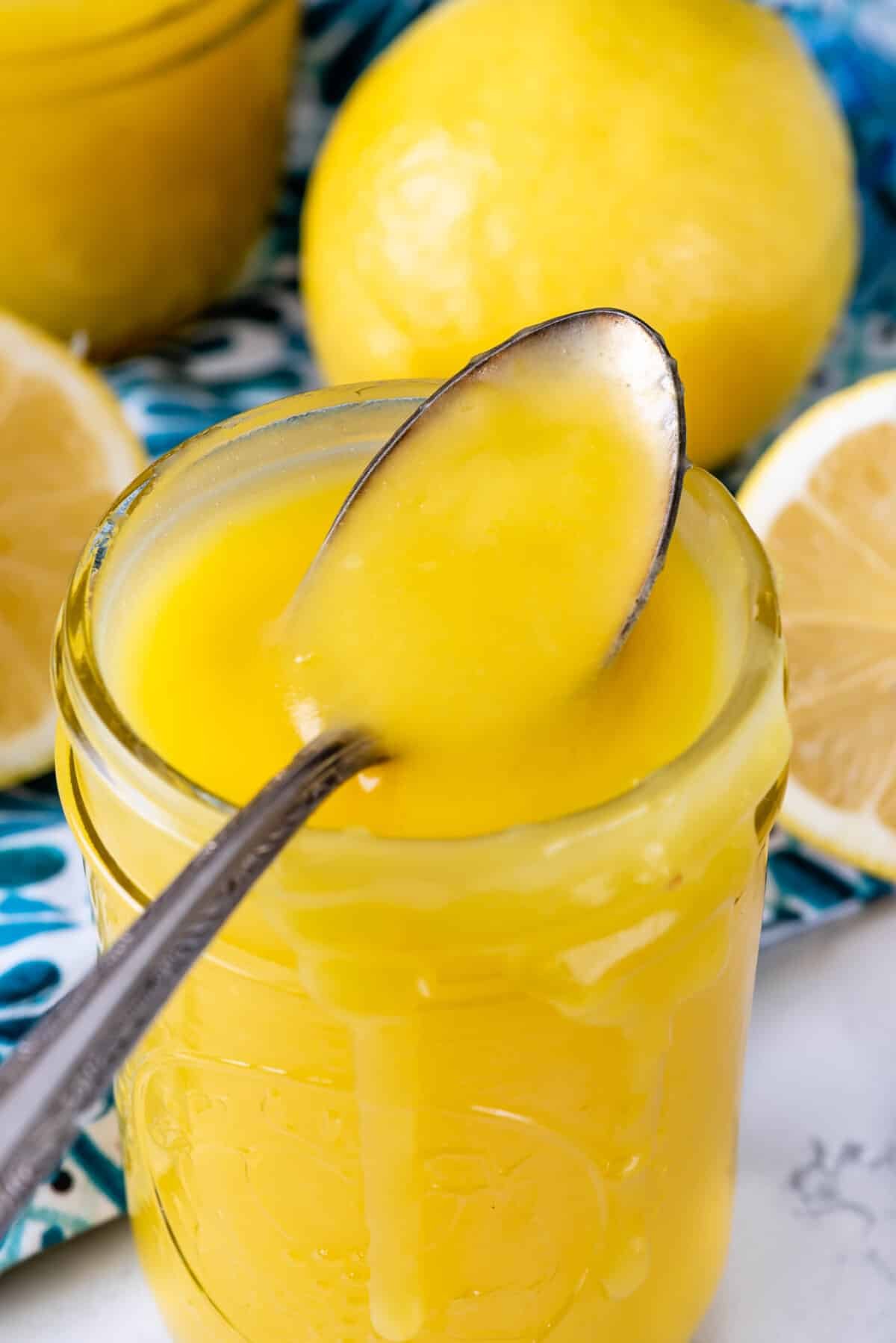 Tall jar of lemon curd with spoon resting on top